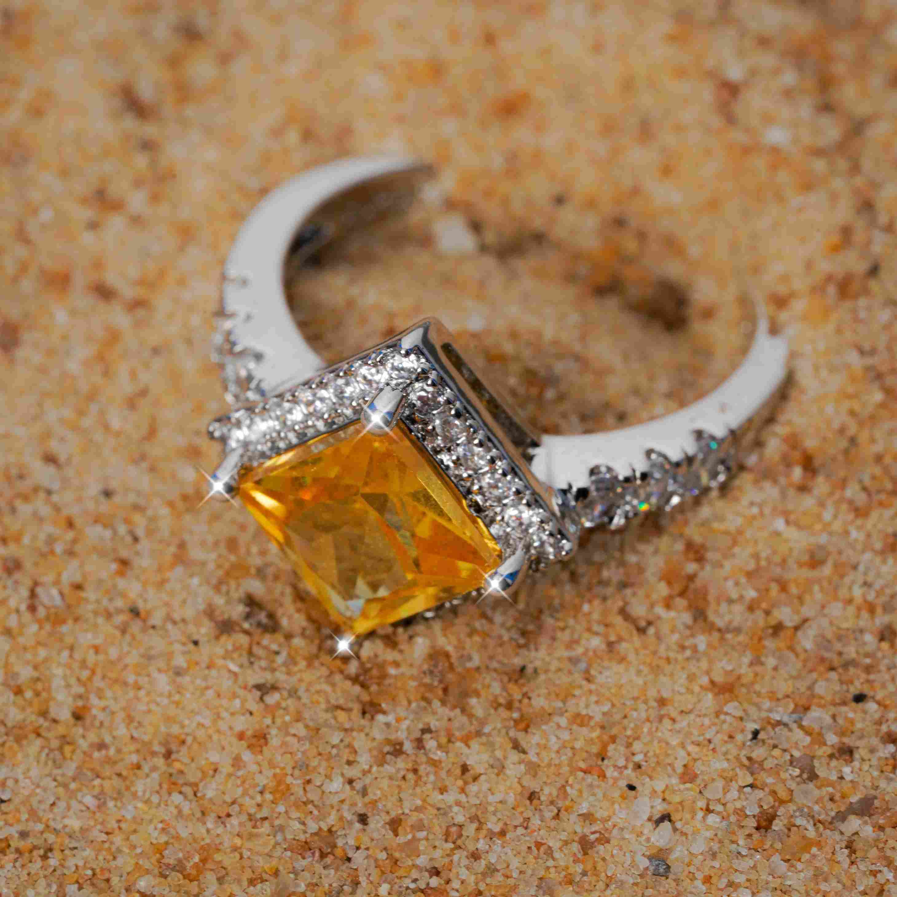Ring with a yellow gemstone and diamond accents on sand