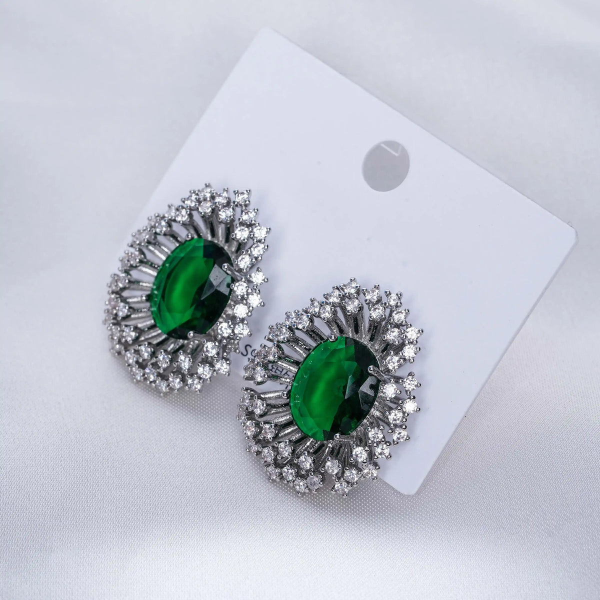 Pair of green gemstone earrings with silver accents on a white card.