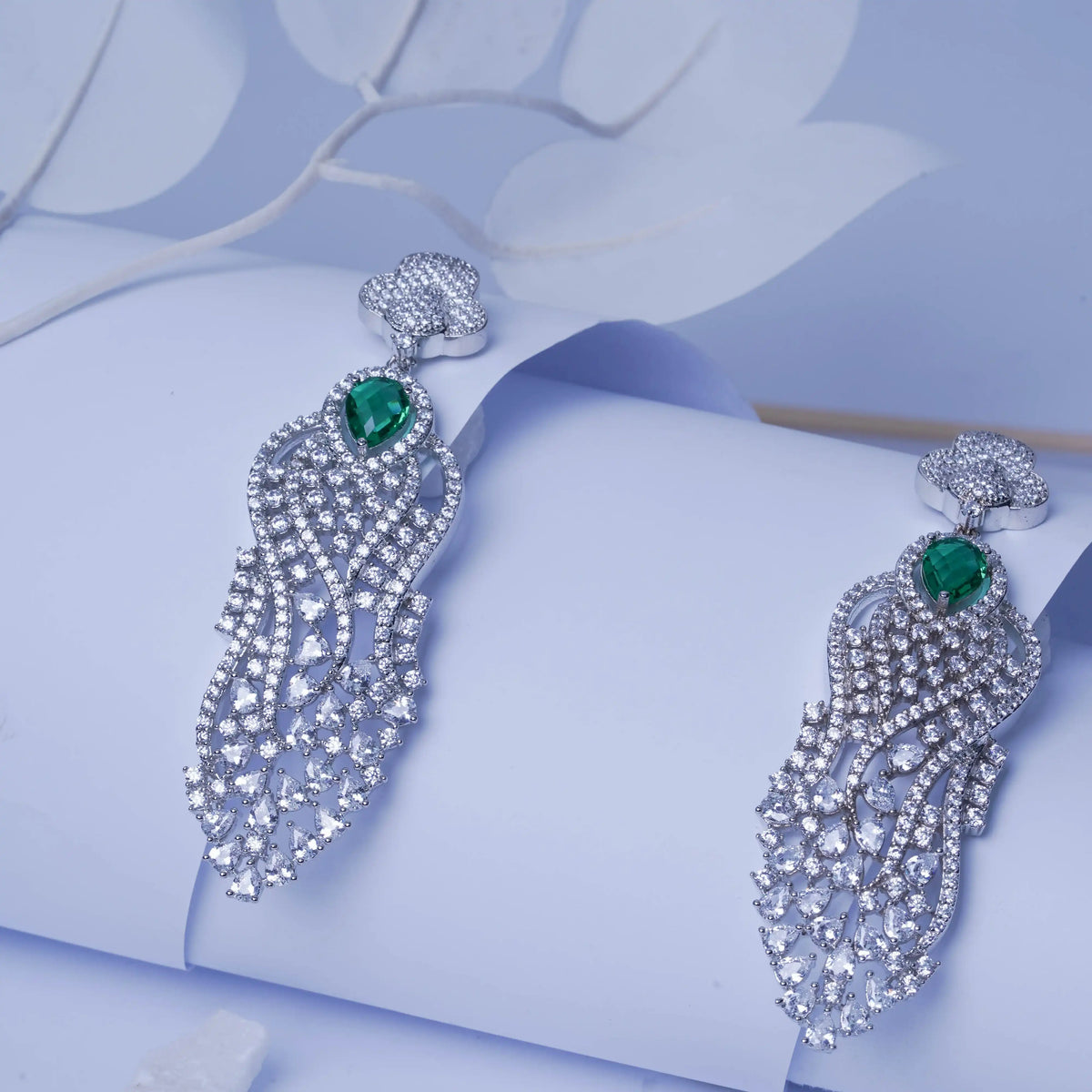 Pair of silver earrings with green gemstones on a light blue floral background