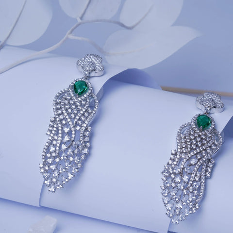 Pair of silver earrings with green gemstones on a light blue floral background