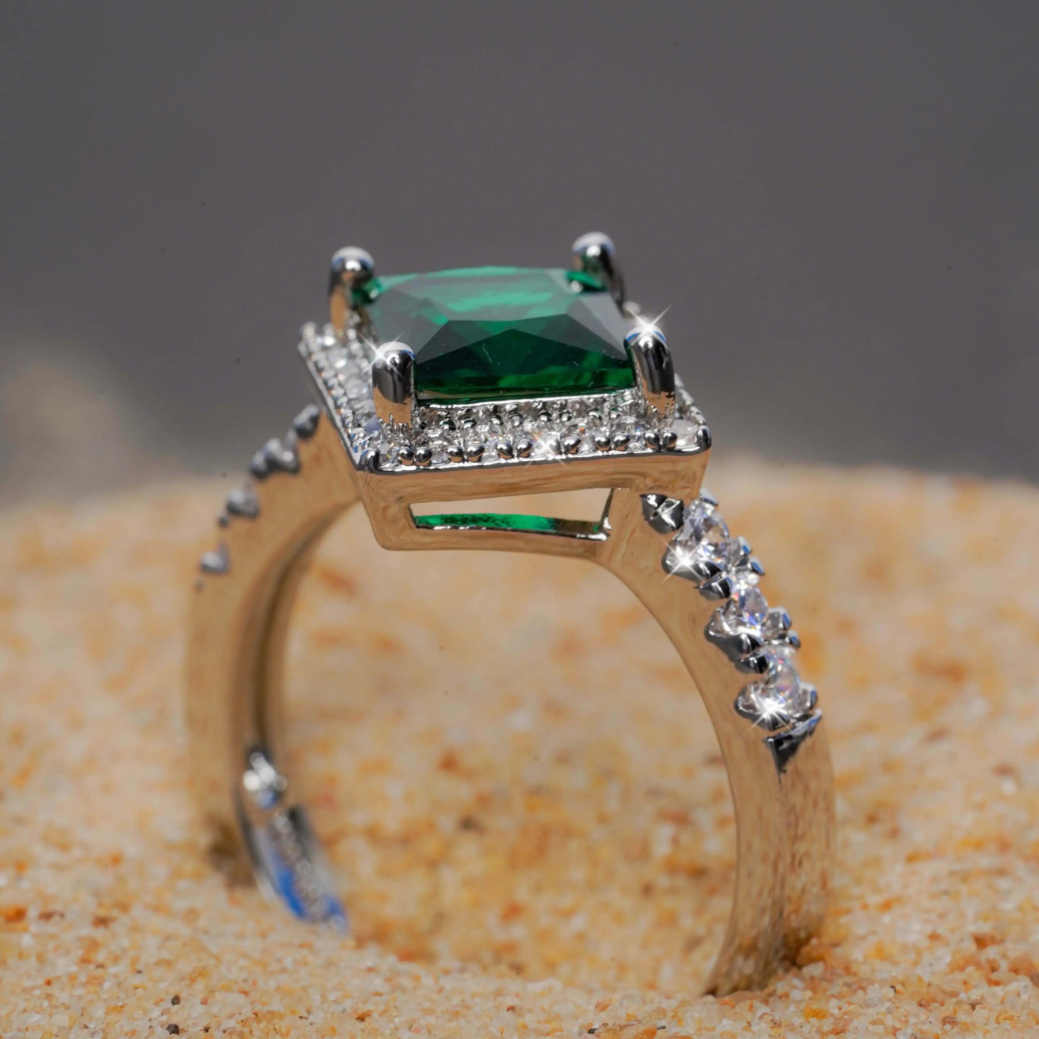 Gold ring with a green gemstone and diamond accents on a sandy background
