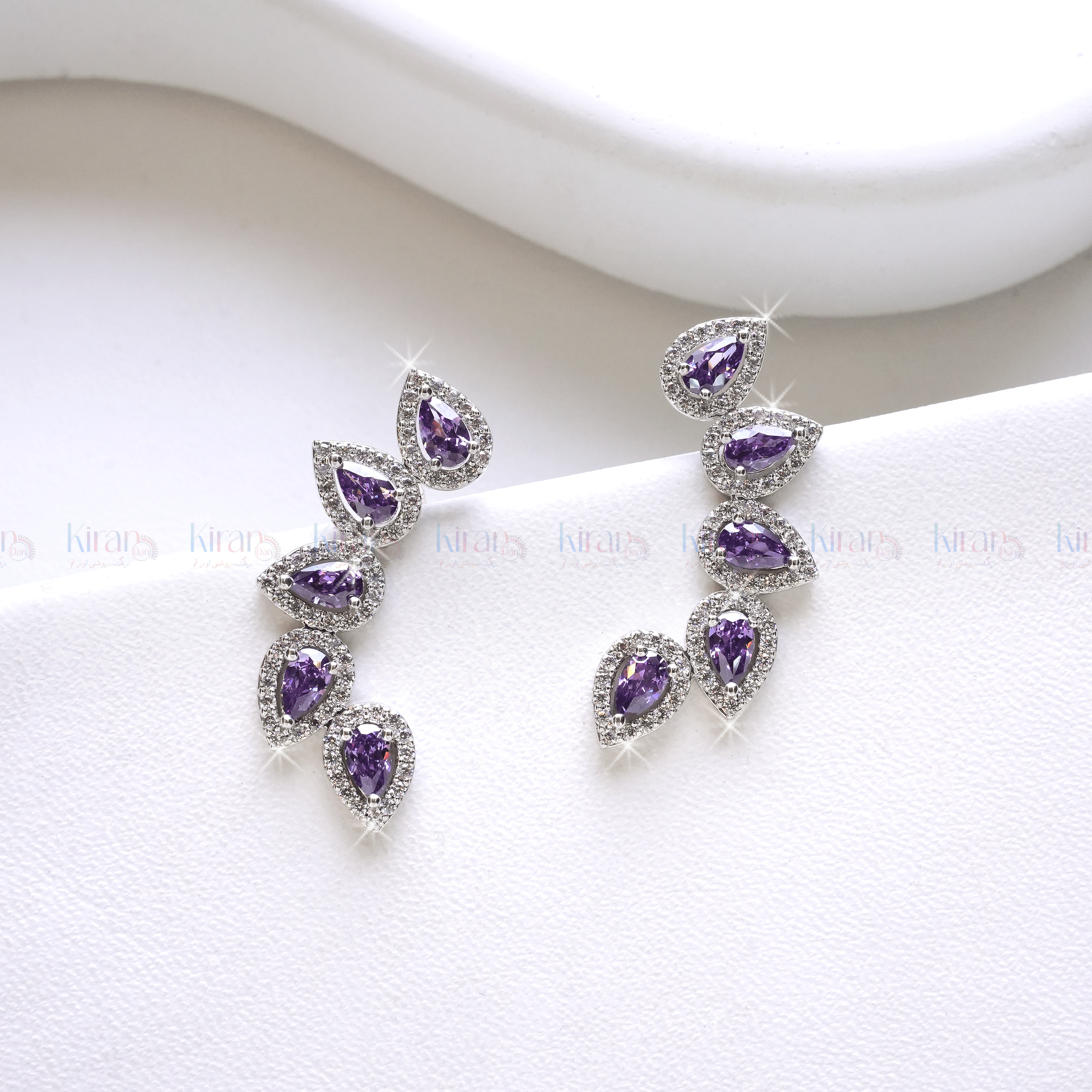 A pair of lavender and white crystal ear climbers on a white surface, showcasing a cascading row of pear-cut lavender stones with white crystal accents.