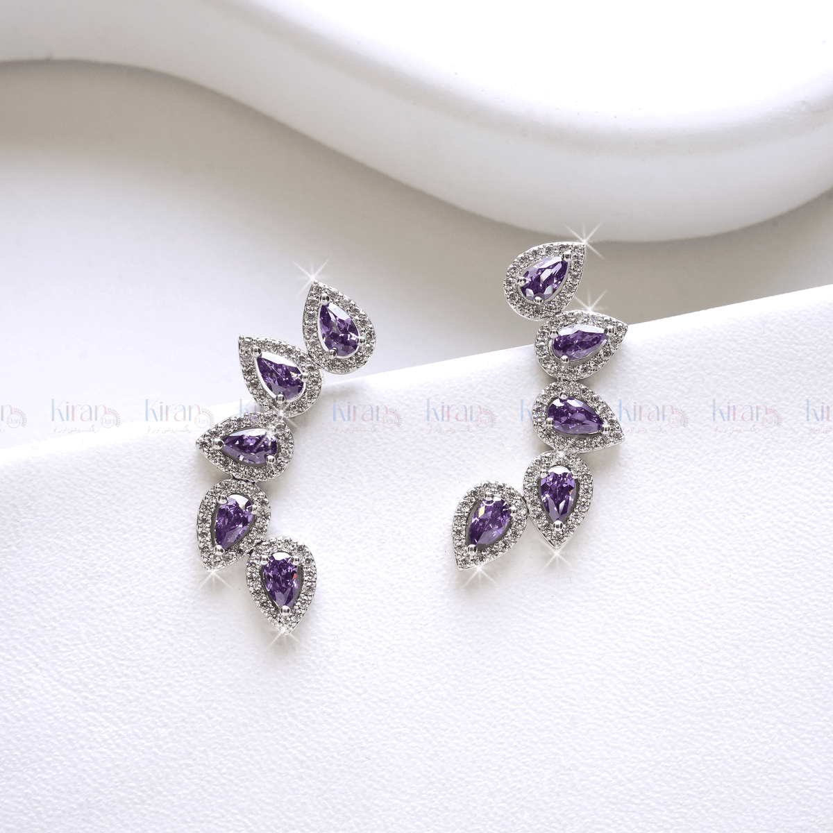 A pair of lavender and white crystal ear climbers on a white surface, showcasing a cascading row of pear-cut lavender stones with white crystal accents.