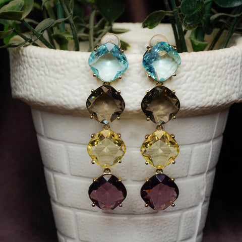 Multicolored gemstone earrings on a white textured surface with plants in the background