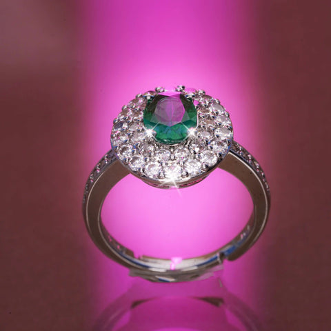 Ring with a green gemstone and diamond accents on a pink background