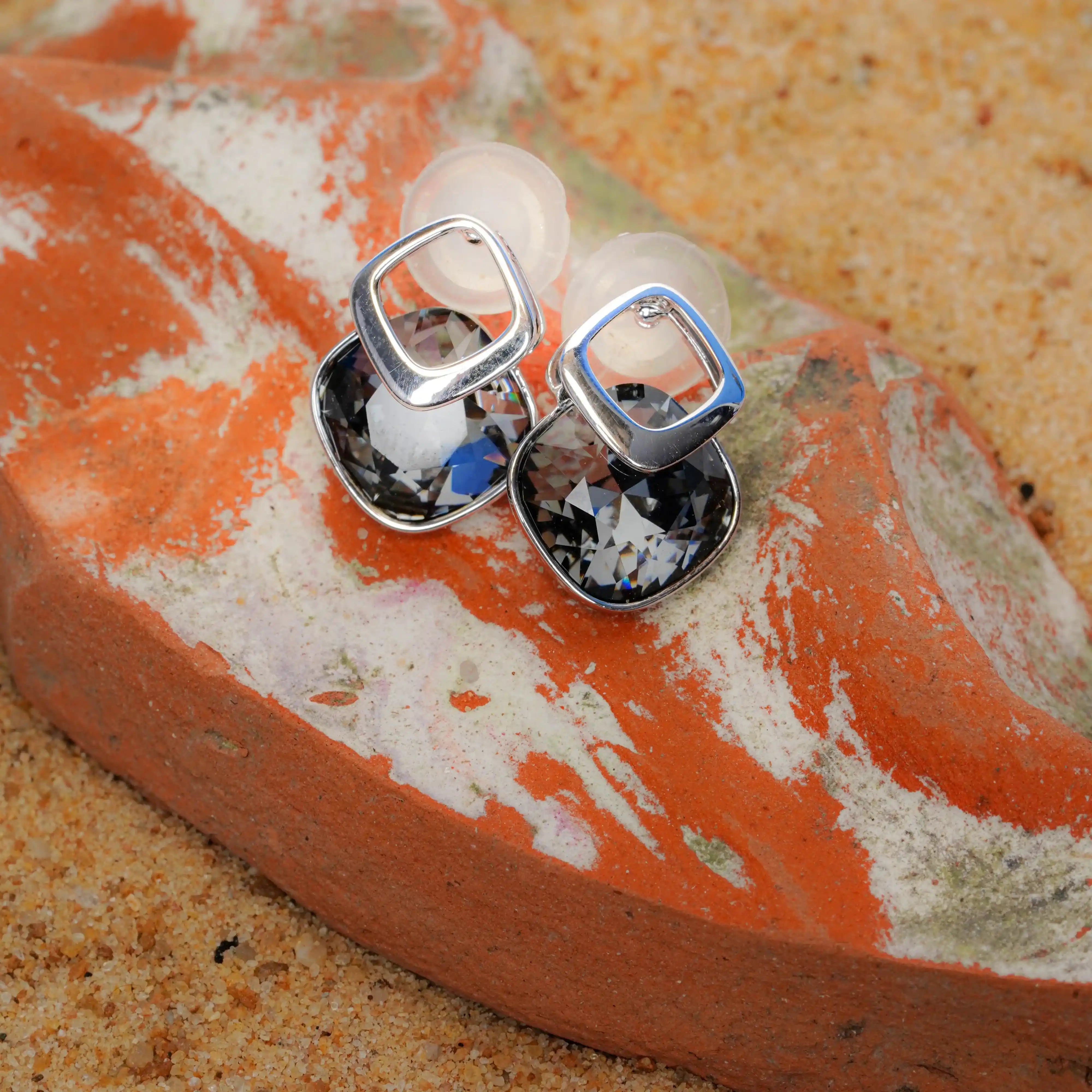 Silver square earrings with gemstones on a textured orange surface
