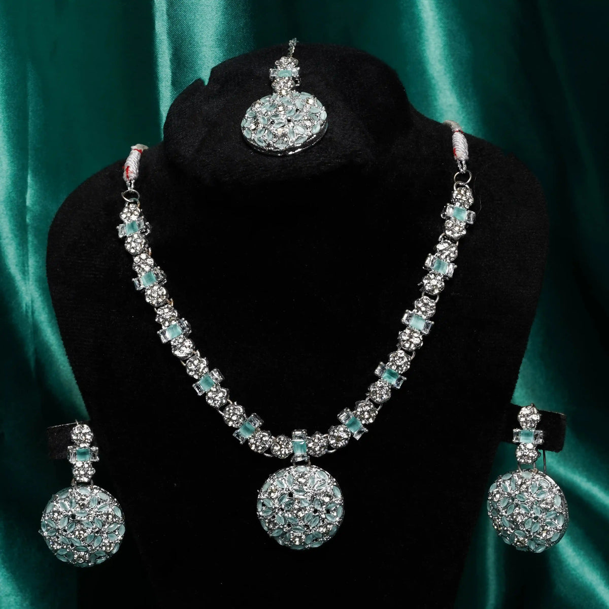 Jewelry set with necklace, earrings, and tikka on a black stand against a green satin background