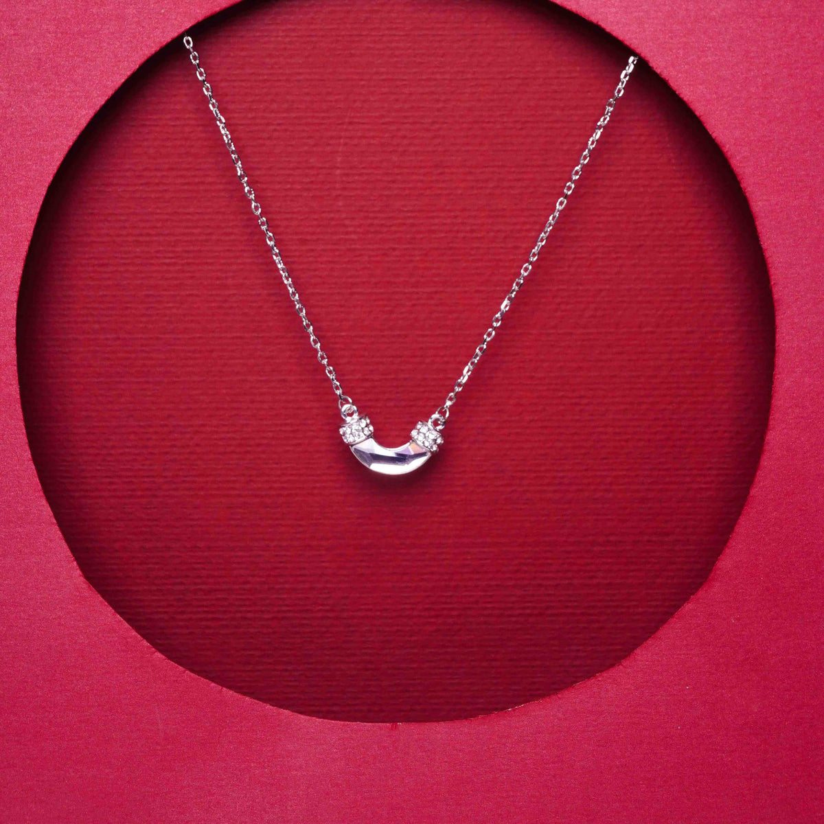 Silver necklace with a crescent moon pendant on a red background