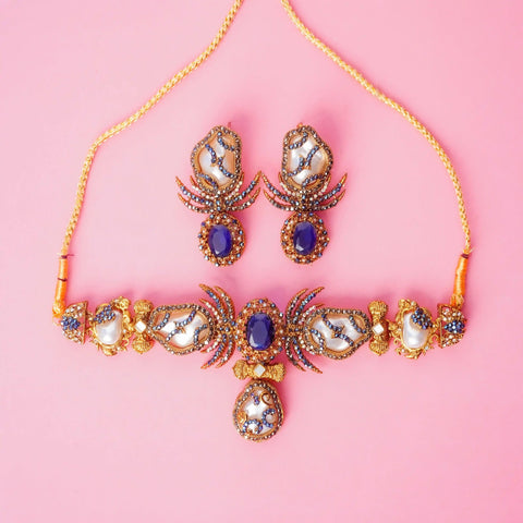 Ornate necklace and earrings on a pink background