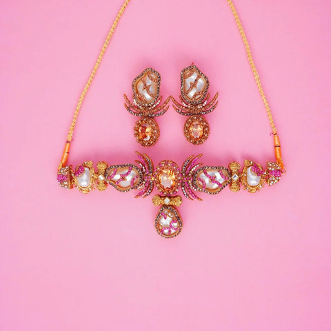 Ornate necklace and earrings on a pink background