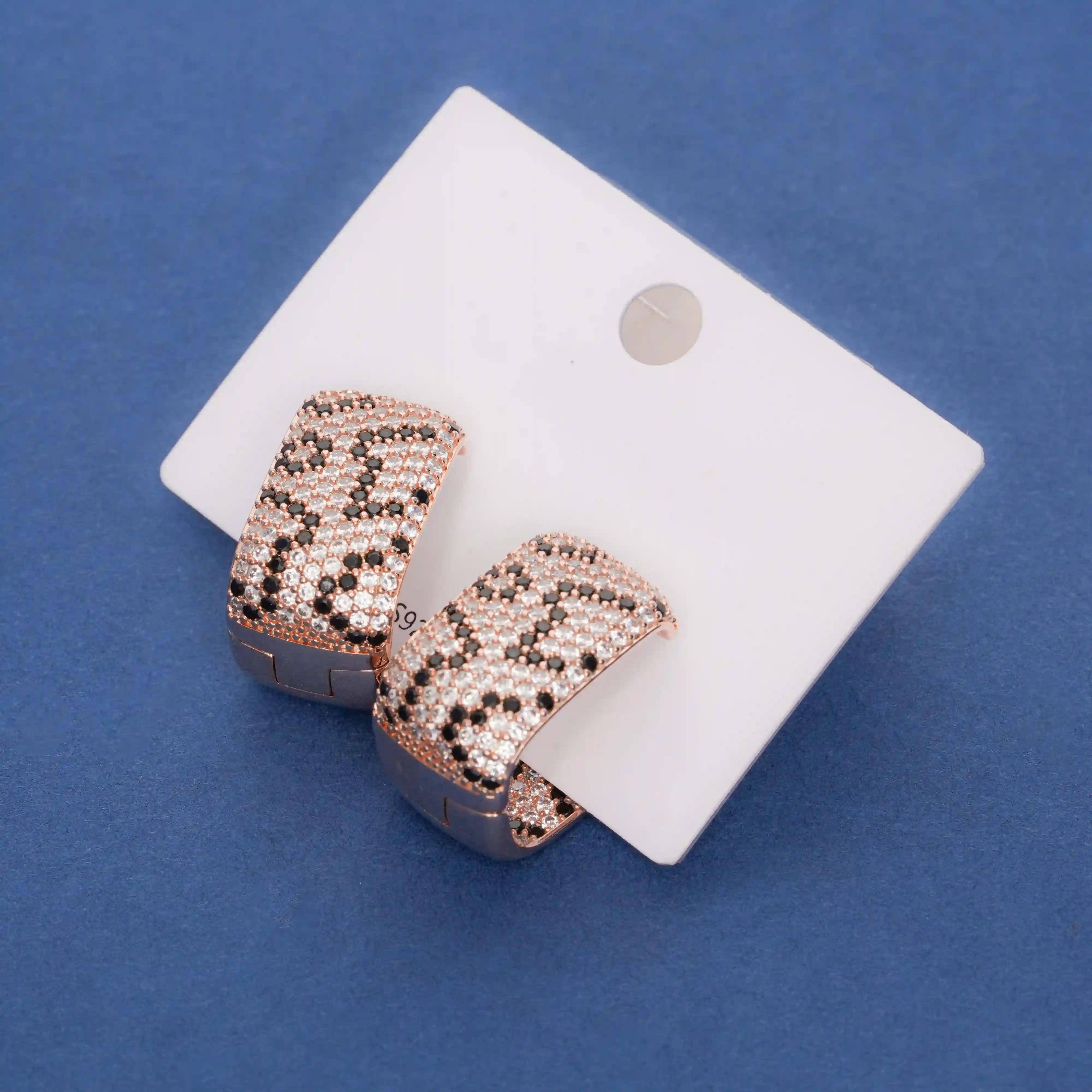 Rose gold heart-shaped earrings on a white card against a blue background