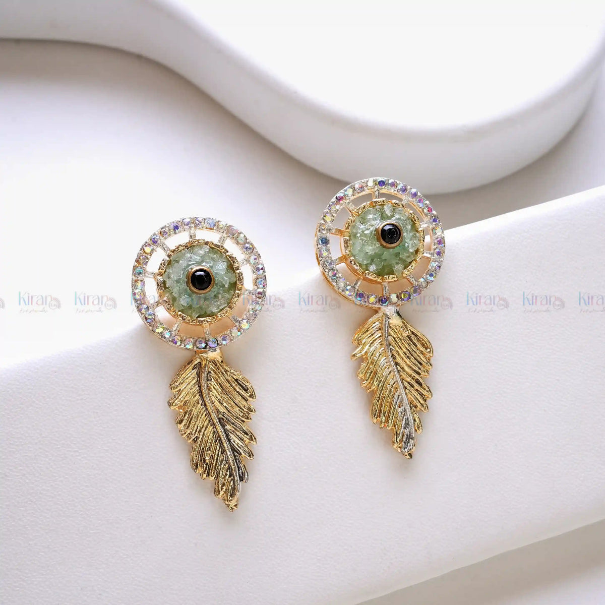 Pair of gold earrings with green crushed stones on a white surface