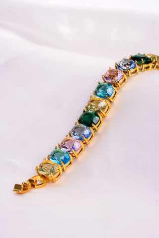 Gold bracelet with multicolored gemstones on a white textured surface