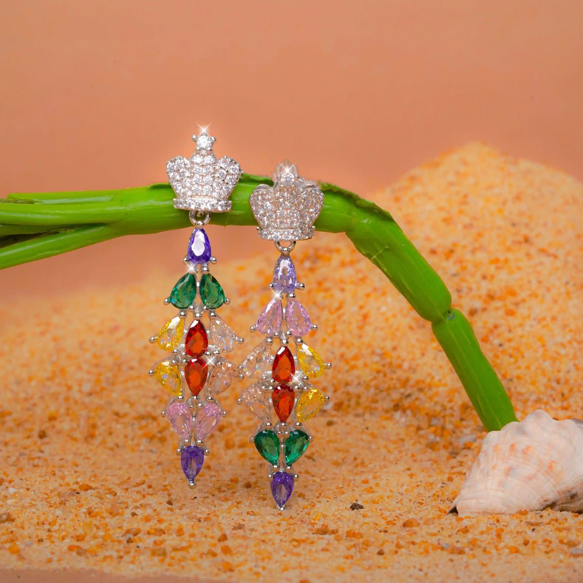 Colorful beaded earrings on a branch with sand and shell background