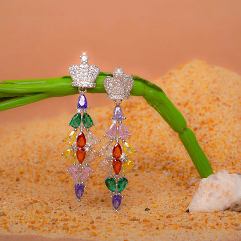 Colorful beaded earrings on a branch with sand and shell background