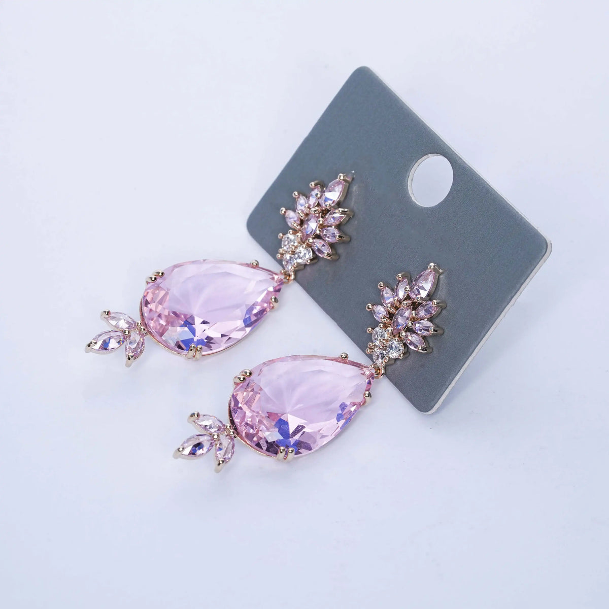 Pink teardrop earrings with gold accents on a gray card against a light blue background