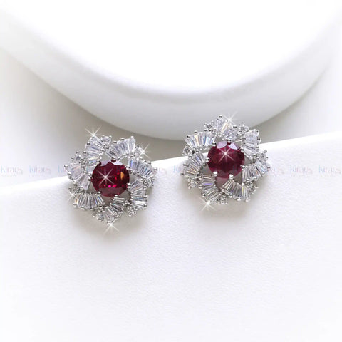 Pair of earrings with red gemstones and diamond-like accents on a white background