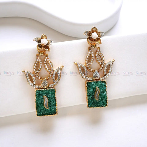 Pair of ornate earrings with green gemstones on a white background