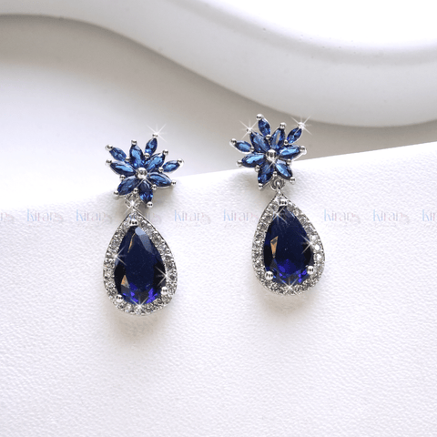 A pair of blue teardrop-shaped earrings with a floral marquise stud design and encrusted with small crystals, displayed against a white background.