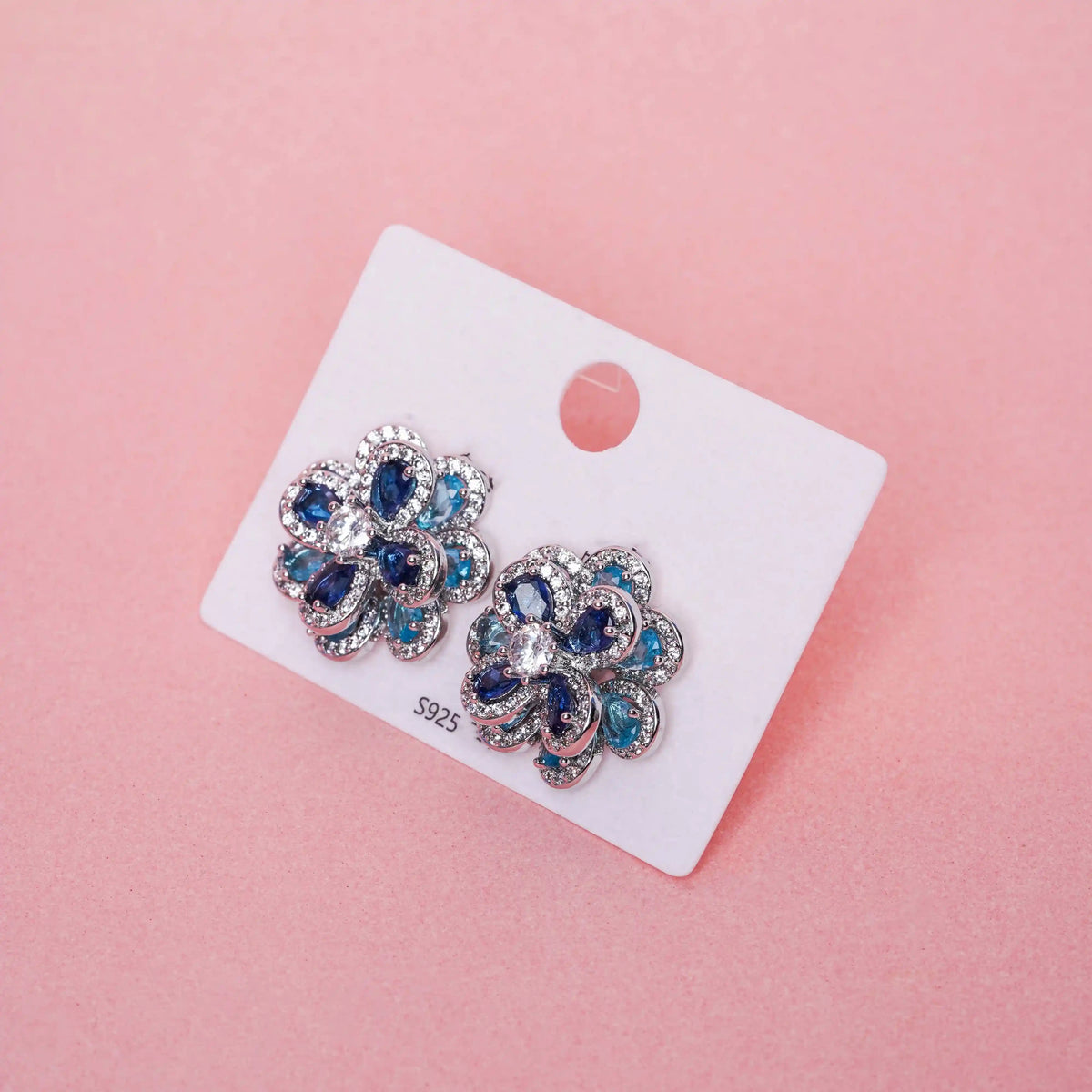 Pair of floral earrings with blue gemstones on a white card against a pink background