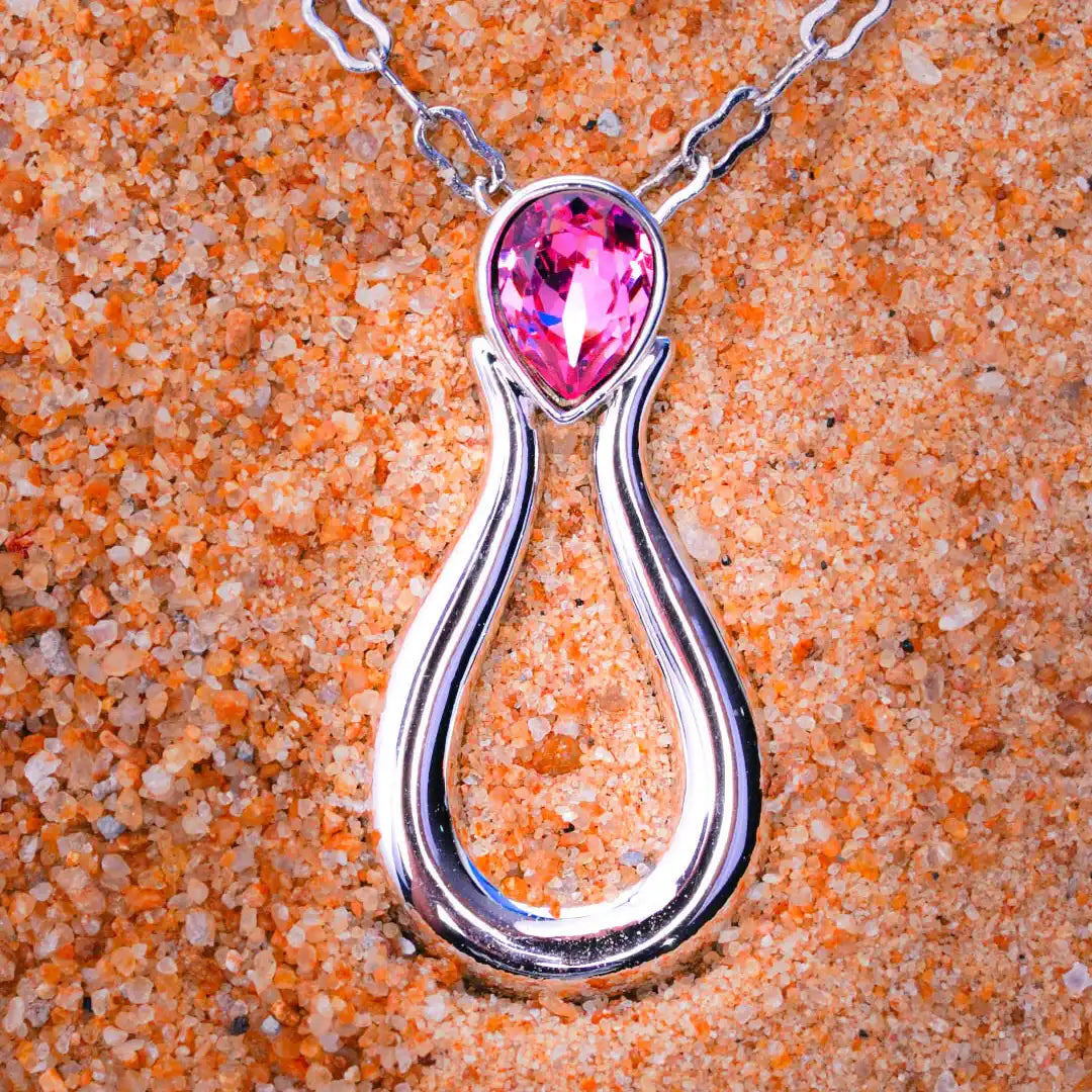 Silver pendant with a pink gemstone on a sandy background