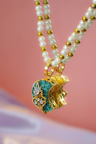 Pearl necklace with a gold and turquoise pendant on a pink background