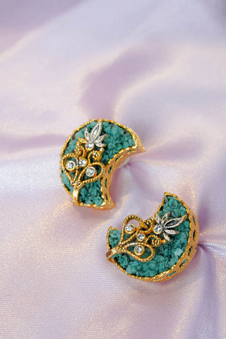 Pair of decorative earrings with green and gold design on a soft pink fabric background