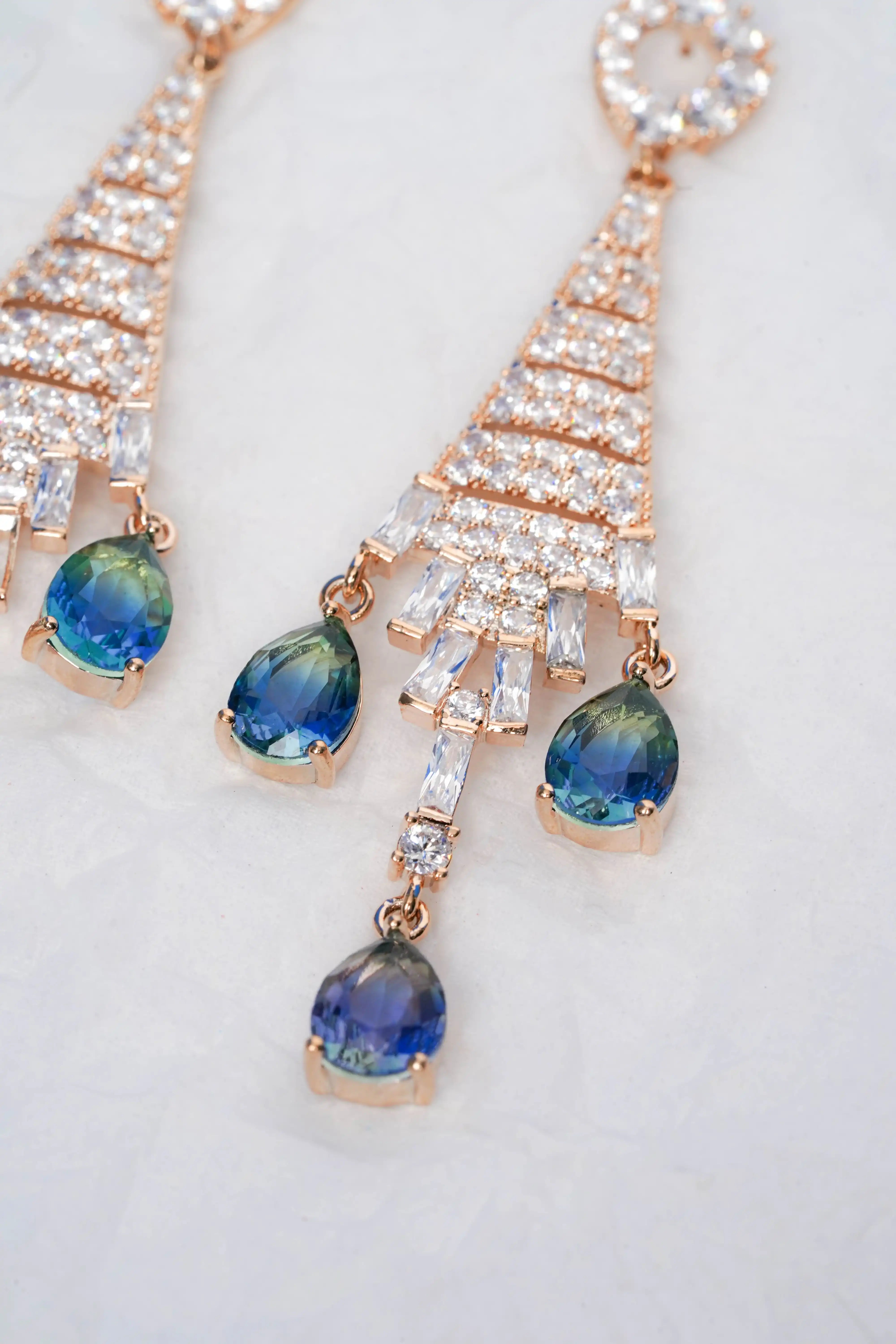 Rose gold earrings with blue gemstones on a white background