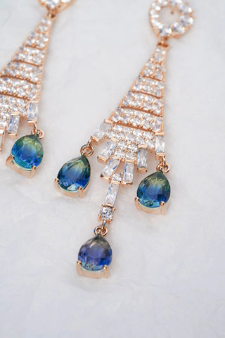 Rose gold earrings with blue gemstones on a white background