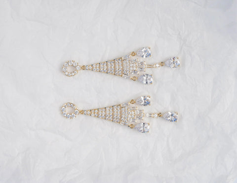 Pair of gold and crystal earrings on a light gray background