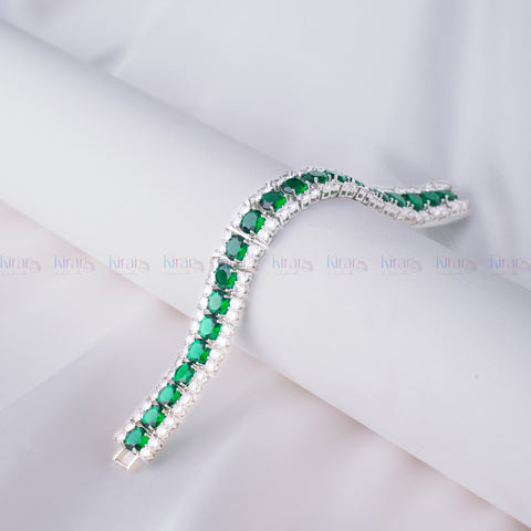 A silver-plated bracelet adorned with emerald-cut green gemstones and small clear accents, displayed on a white surface.