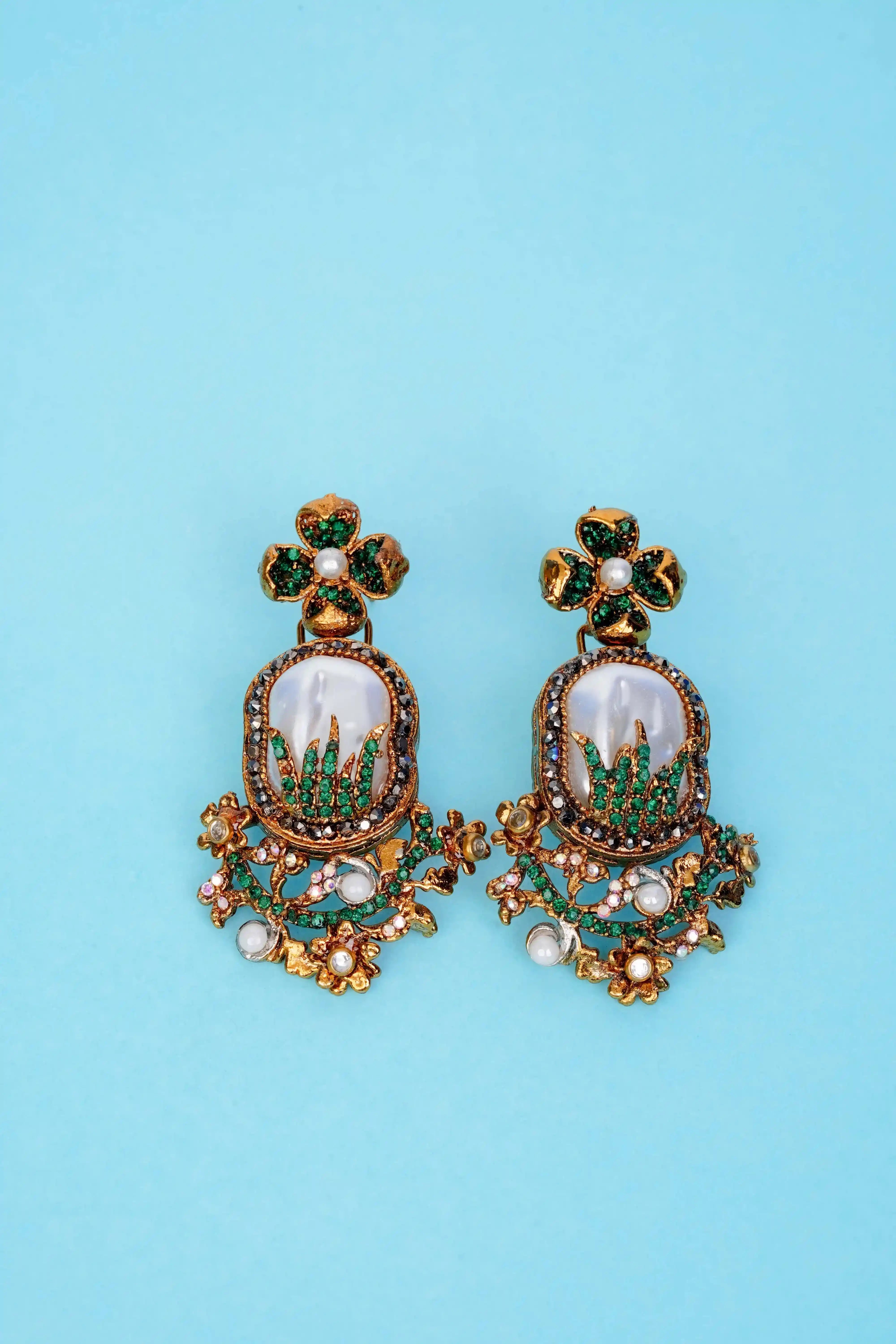 Ornate earrings with green and gold details on a blue background