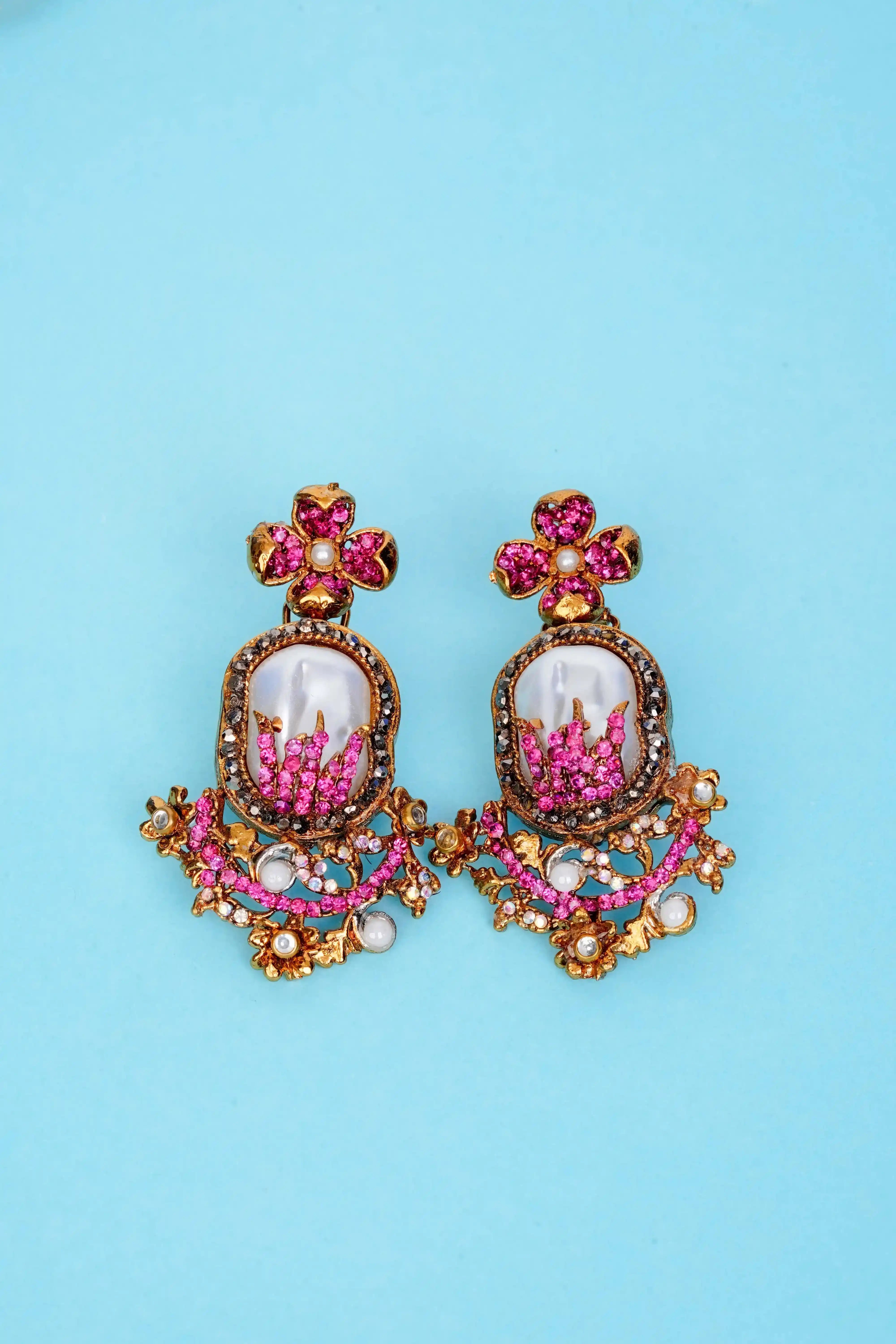 Pair of ornate earrings with pink and gold details on a blue background