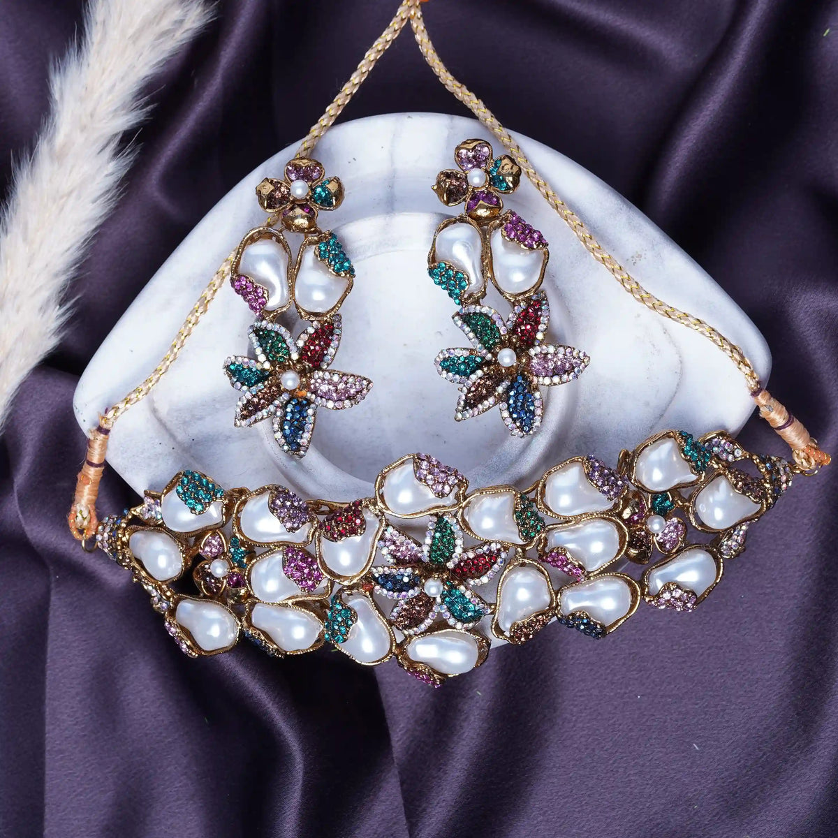 Ornate necklace and earrings on a white stone with a purple fabric background