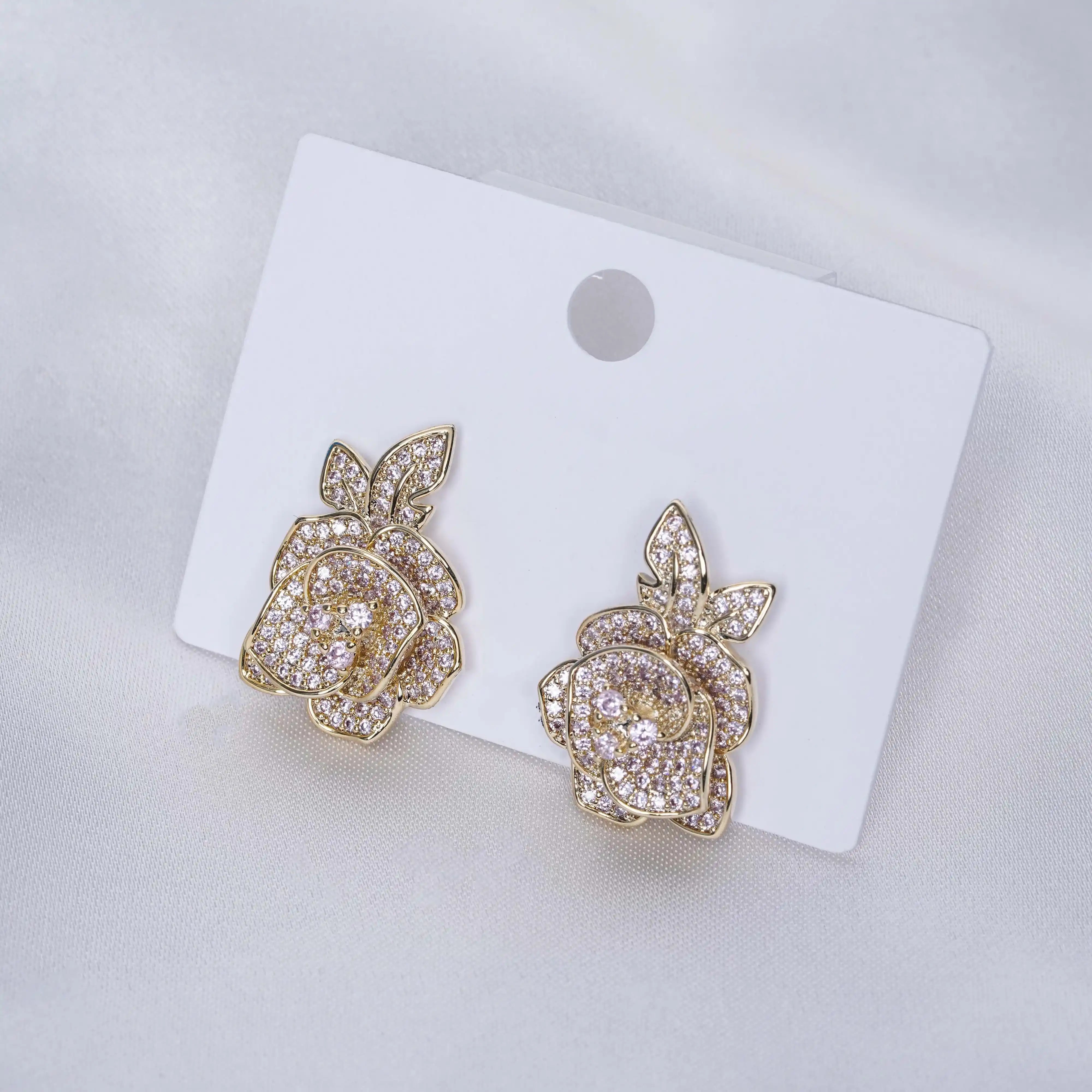 Gold rose-shaped earrings on a white card with a gray background