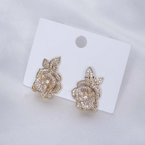 Gold rose-shaped earrings on a white card with a gray background