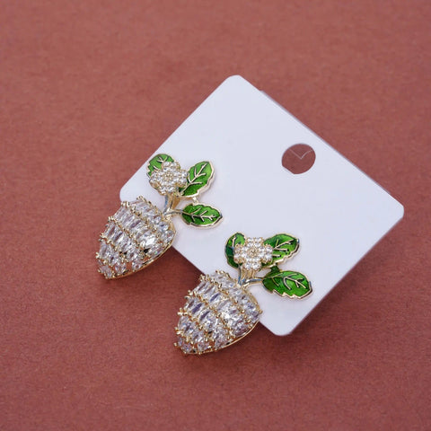 Pair of pineapple-shaped earrings with green leaves on a white card against a brown background