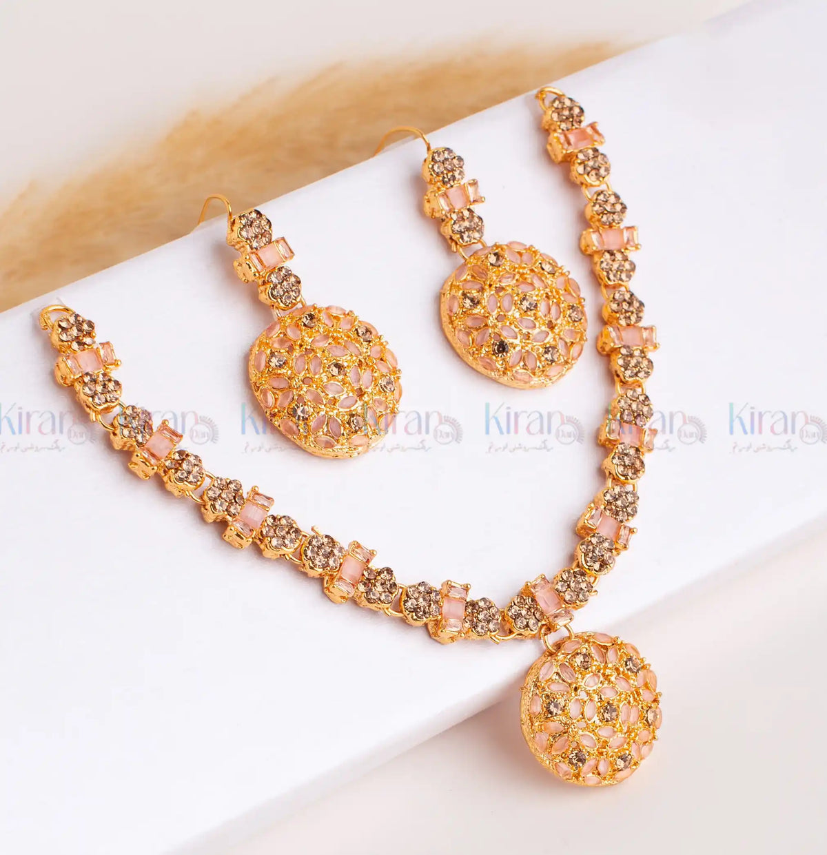 Ornate necklace and earrings set on a white surface with 'Kiran' branding.