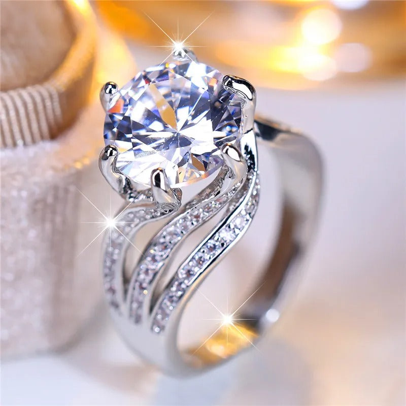 A silver ring with a large central gemstone and smaller stones in the band, displaying a lot of sparkle.